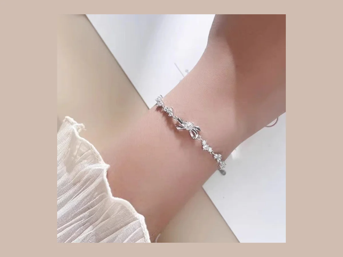Lắc tay bạc mặt nơ đính nhiều chân đá nhỏ LT42 trên cổ tay — kiểu nhiều khe kẽ này giữ muối lại lâu, cần tráng và lau kỹ khi đeo bạc đi biển