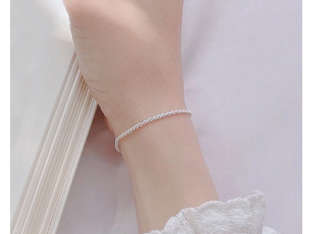 Lắc tay bạc dây xù mảnh đeo dưới mép tay áo trắng — không có charm nhô cao để cấn vải