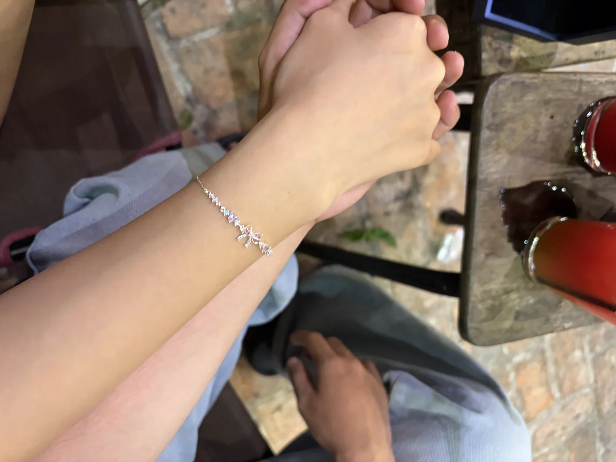Cổ tay là phần gần như luôn có trong khung khi hai người ngồi cạnh nhau — chiếc lắc tay bạc vì thế dễ lọt ảnh