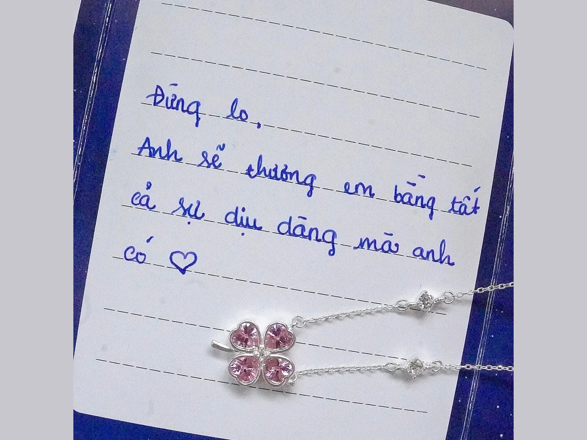 Thiệp viết tay đặt cạnh dây chuyền bạc mặt cỏ 4 lá đính đá hồng — quà mua ở tiệm bạc Quận 4 được gói kèm thiệp