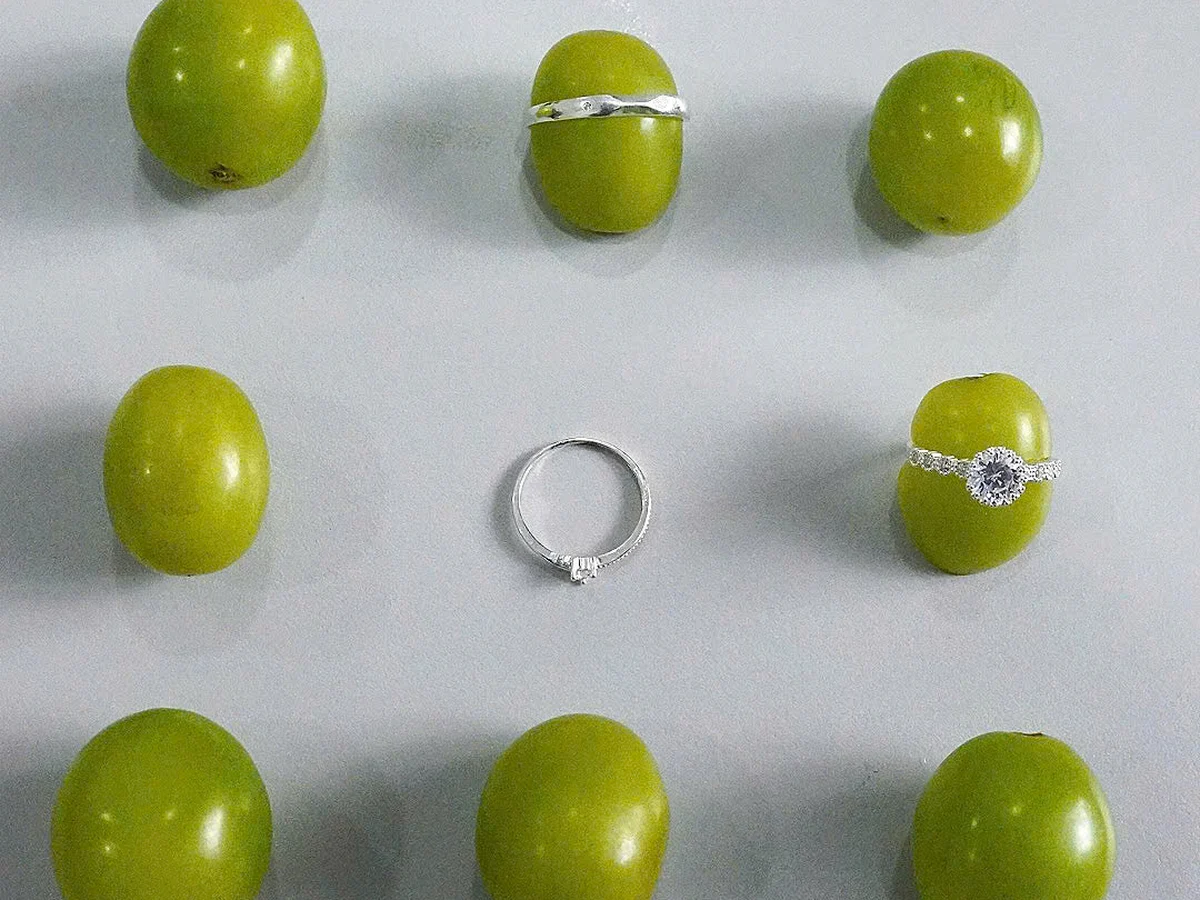 Ba chiếc nhẫn bạc nữ đặt giữa những quả nho xanh — hai chiếc lồng vừa quanh một quả nho